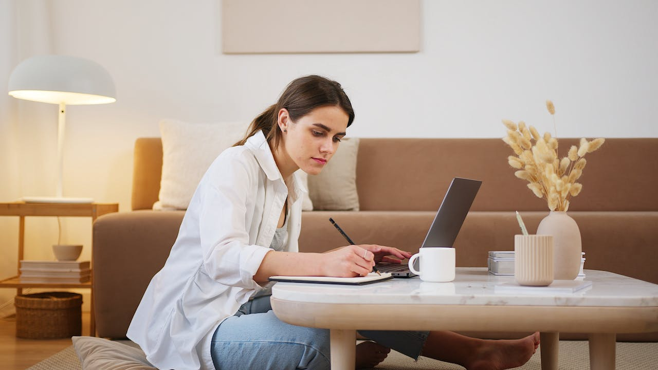 a young woman using laptop and taking down notes